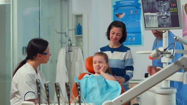 Bambino usando il dito per puntare il dente colpito mentre il dentista parla con la madre — Video Stock