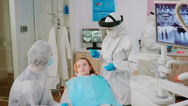 Odontólogo pediátrico en escudo protector comprobando dientes de niña — Vídeo de stock