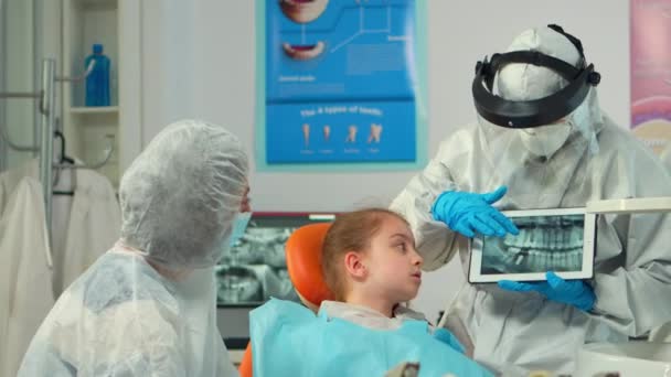 Dentist in protective equipment showing on tablet dental x-ray of child — Stock Video