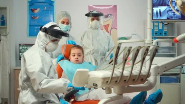 Dentista pediatrico in tuta protettiva che accende la lampada fino all'esame — Video Stock