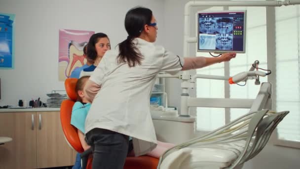Stomatologo che indica sullo schermo digitale spiegando i raggi X alla madre — Video Stock