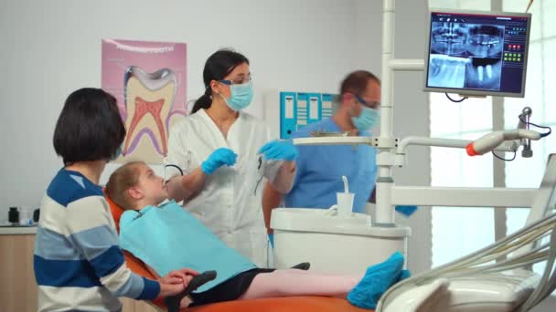 Enfermeira pediátrica e médico dentista trabalhando na clínica odontológica moderna tratando menina — Vídeo de Stock