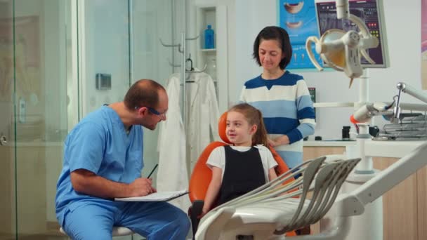 Vriendelijke man tandarts assistent ondervragen kind patiënt — Stockvideo