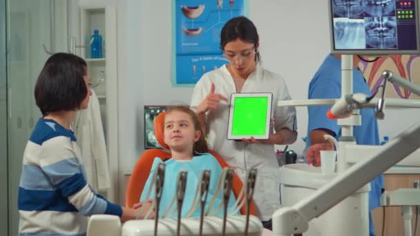 Детский стоматолог, стоящий рядом с пациенткой, указывая на зеленый экран — стоковое видео