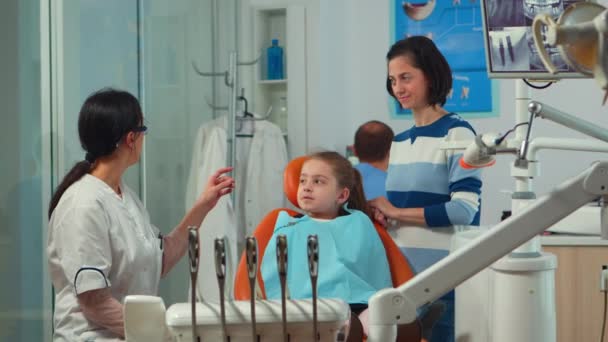 Mulher pediátrica dentista tratando menina paciente em consultório estomatológico — Vídeo de Stock