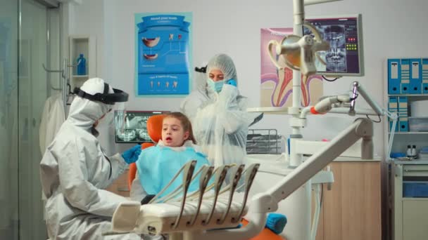 Dentista pediatrico che indossa tuta protettiva che tratta paziente ragazza — Video Stock