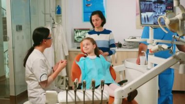 Stomatolog küçük kıza diş temizleme işlemini açıklıyor.