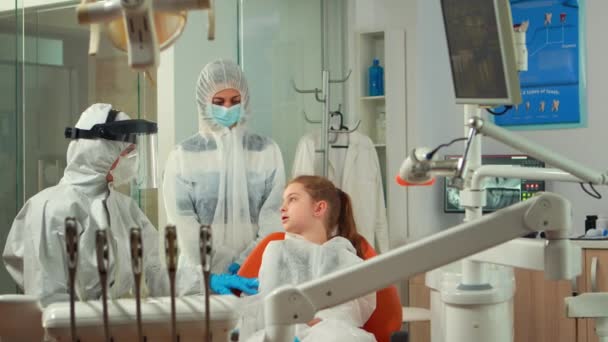 Dentistry nurse in coverall putting dental bib to child before examination — Stock Video