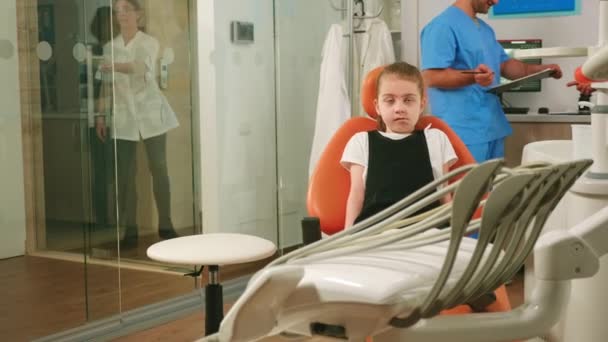 Paziente bambina in attesa di stomatologa pediatrica donna seduta sulla sedia dentale — Video Stock