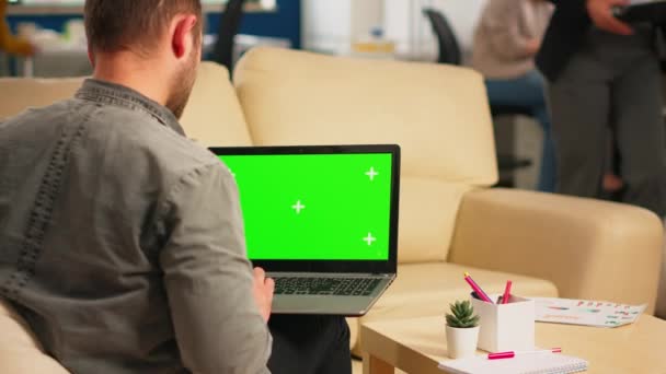 Вид на бизнес-человека, сидящего на диване с помощью ноутбука с зеленым экраном — стоковое видео