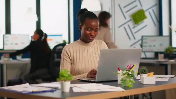 Happy black manager czytanie zadań na laptopie i pisanie siedzi na biurku — Wideo stockowe