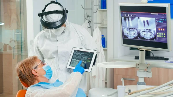 Stomatologo con schermo facciale che rivede i raggi X che puntano sul tablet — Foto Stock