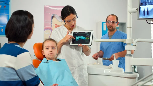 Стоматолог указывает на цифровой экран, объясняя рентген матери — стоковое фото