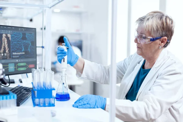 Senior genetic researcher taking sample from glass flask — Stock Photo, Image