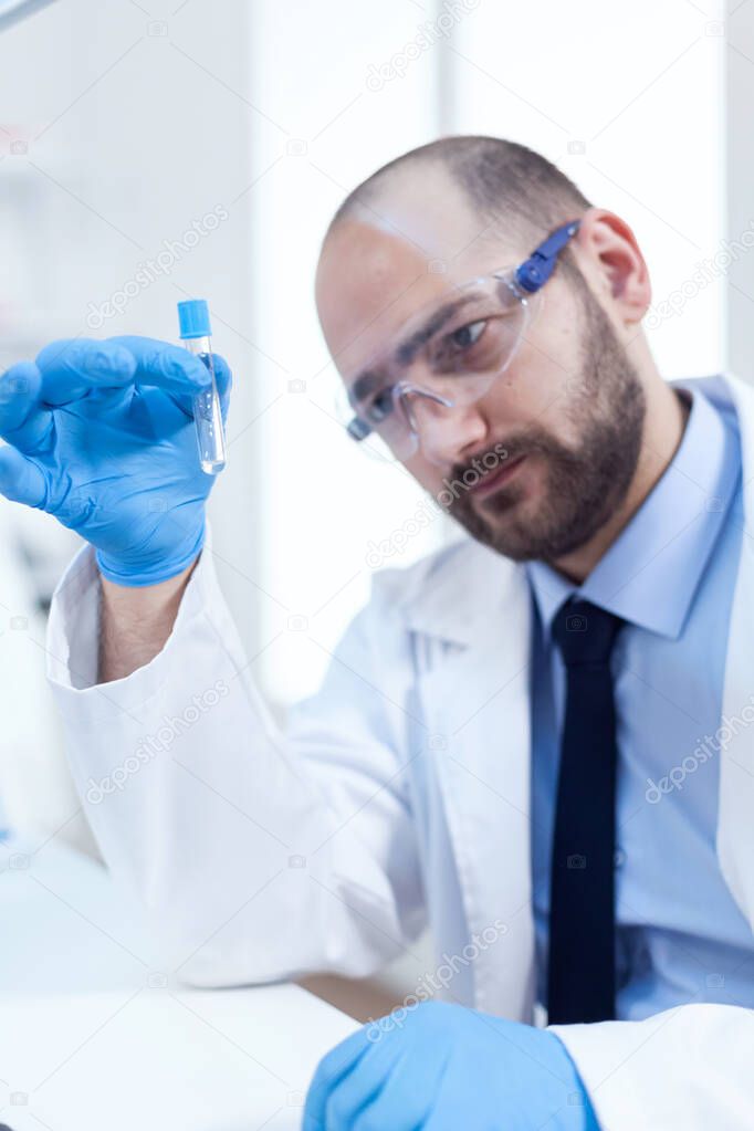 Male scientist with sterile gloves looing at test tube