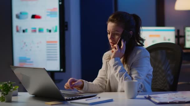Жінка-працівник розмовляє по телефону під час роботи на ноутбуці — стокове відео