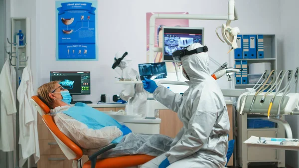 Odontologista em kit de proteção individual examinando raio-X dental — Fotografia de Stock