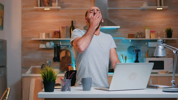 Hombre cansado bostezando mientras trabaja desde casa tarde en la noche — Foto de Stock