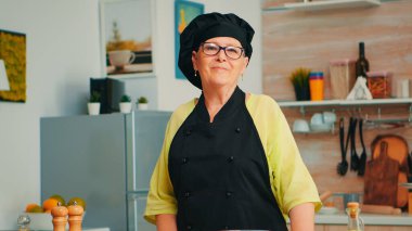 Yaşlı kadın şef önlüğü giyiyor.