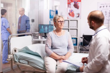 Yaşlı kadın hastane dolabında doktorla konuşuyor.