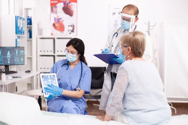 Sjuksköterska och läkare diskuterar med äldre kvinna patient — Stockfoto