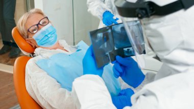 Yüz kalkanı olan doktor panoramik diş röntgeni görüntüsünü inceliyor