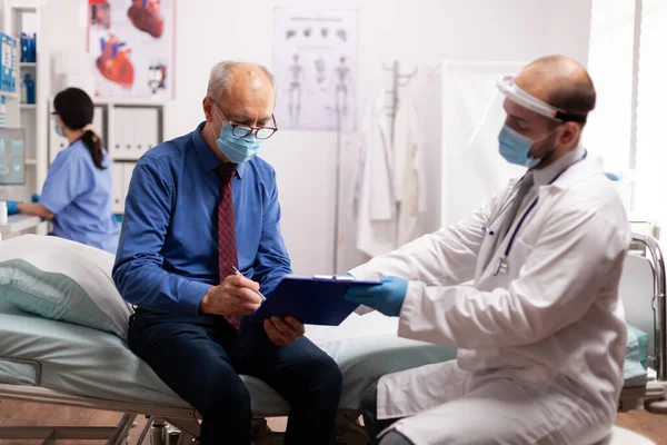 Elderly patient wearing face mask reading paperwork — Stock Photo, Image