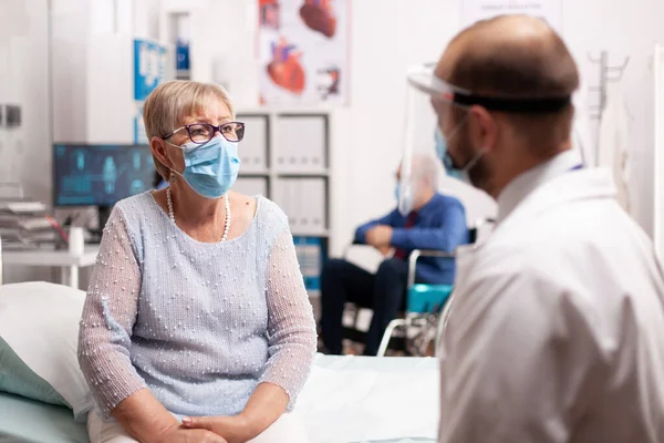 Preoccupata donna anziana con maschera viso guardando il medico — Foto Stock