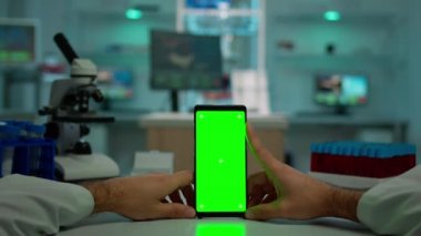 Kimyagerin yeşil ekranlı akıllı telefonu kullanırken ki görüntüsü.