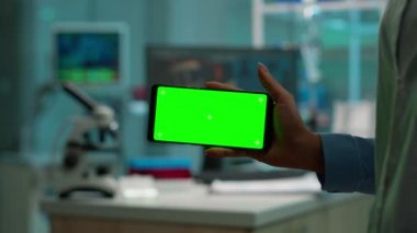 Yeşil modelli yatay telefonu tutan bilim adamının yakın plan fotoğrafı.