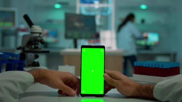 Pov πλάνο του μικροβιολόγου κρατώντας τηλέφωνο με πράσινο chroma βασική οθόνη — Αρχείο Βίντεο