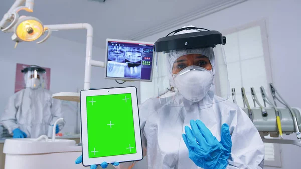 Доктор в костюме ppe показывает планшет с зеленым экраном — стоковое фото