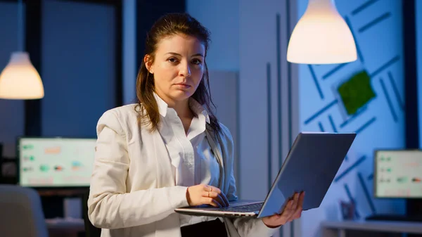 Gerente mujer sosteniendo el ordenador portátil, escribiendo y mirando satisfecho en la cámara — Foto de Stock