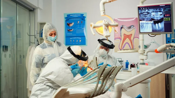Zahnarzt im Schutzanzug mit sterilisierten Zahnwerkzeugen bei der Untersuchung eines kleinen Patienten — Stockfoto