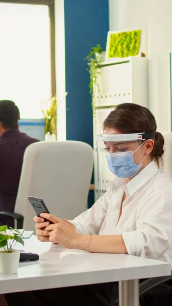 Деловая женщина в маске чата с помощью телефона в офисной комнате — стоковое фото