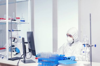 Steril takım elbiseli araştırmacı iş yerinde oturuyor.