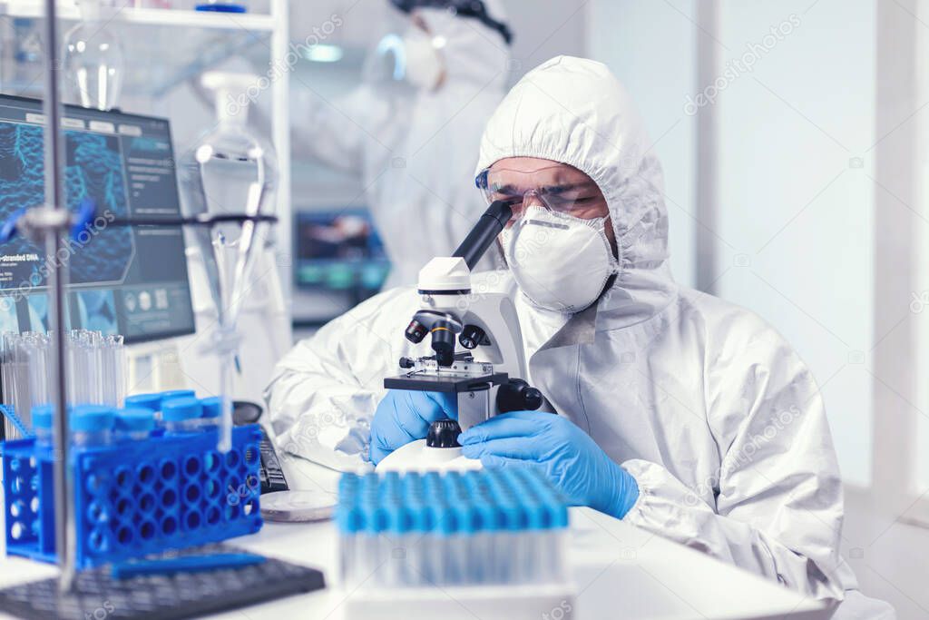 Lab technician in ppe gear examining virus samples under microscope