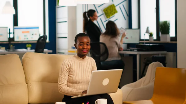 Afrikansk amerikansk dam skriver på laptop tittar på kameran leende — Stockfoto