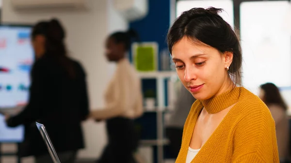 Jeune femme travaillant à un ordinateur portable assis au bureau dans une start-up financière occupée — Photo