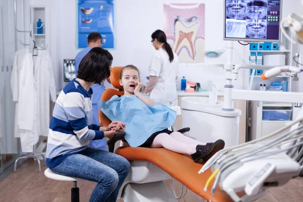 Little girl in dentist office touching mouth with hand and painfull expression Stock Image