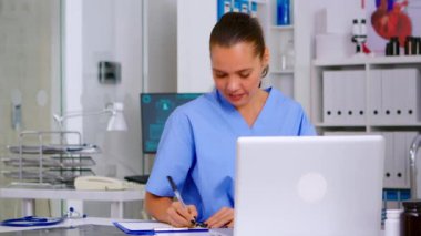 Hemşire laptoptan tıbbi raporları okuduktan sonra not alıyor.