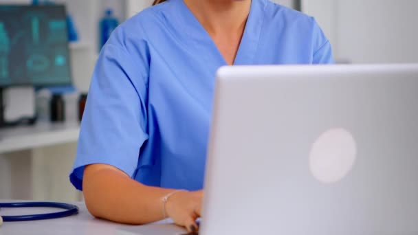 Close up of young medical assistant typing at laptop and raising head smiling — Stock Video