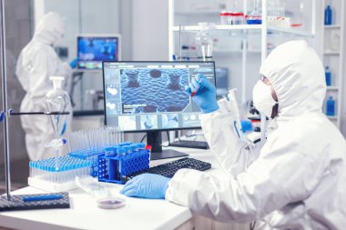 Yüz maskeli ve koylu tıp mühendisi kan örneğine bakıyor.