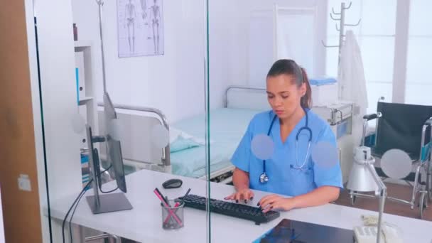 Médico assistente digitando no computador com um monitor sentado atrás de uma parede de vidro — Vídeo de Stock