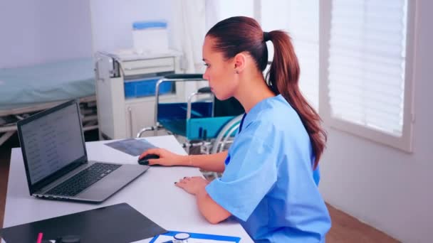 Infermiera di medico digitando sul computer portatile seduto alla scrivania nel gabinetto — Video Stock