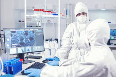 Koruma giysisindeki hemşire laboratuvar teknisyeniyle konuşuyor.