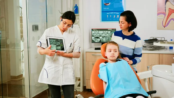 Doctor holding tablet with x-ray showing it to mother of girl patient