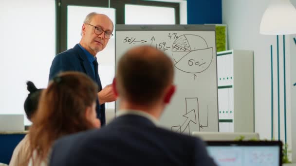 Äldre affärsman ger presentation till multietniskt team med blädderblock — Stockvideo