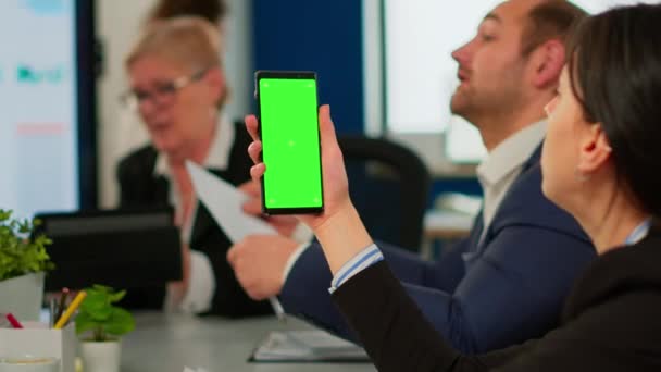 Geschäftsleute analysieren Berichte am Schreibtisch sitzend, während Mitarbeiter ihr Telefon mit grünem Bildschirm halten — Stockvideo