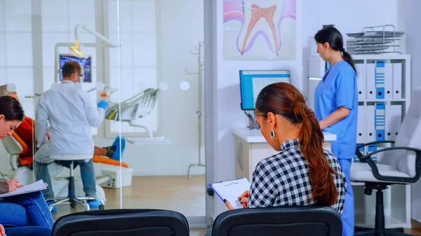 Обратный вид женщины, заполняющей стоматологический документ, сидящей на чиаре — стоковое фото